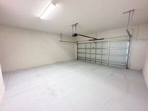 A clean, empty garage with a closed metal door, fluorescent lighting, and a ceiling-mounted light fixture. - 211mcv - Balmoral Resort 6 Bedroom Home (Haines City)