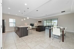A spacious kitchen with a central island, a dining area with a white table and chairs, and a living area with a sofa and TV. - 211mcv - Balmoral Resort 6 Bedroom Home (Haines City)