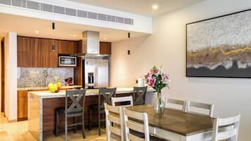 Una cocina moderna con encimeras de granito, armarios de madera y electrodomésticos de acero inoxidable. Hay un comedor con una mesa y sillas de madera, y un florero con flores sobre la mesa.