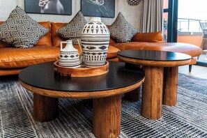 Ein modernes Wohnzimmer mit einem Ledersofa, zwei runden Holztischen mit schwarzen Platten und dekorativen Vasen auf einer Holztablett.