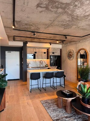 A modern kitchen with a central island, bar stools, and a dining area with a round table. - The Outlook - Luxury Living Above Cape Town (Cape Town)