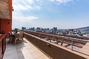 Eine Dachterrasse mit Blick auf die Stadt, einem Tisch mit Stühlen und einem Blumentopf.