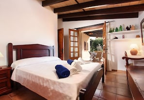 A bedroom with a wooden bed, a nightstand, a table with a lamp, and a view of the outdoors. - Villa 'Juanito' with Private Pool, Wi-Fi and Air Conditioning (Illes Balears)