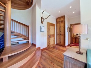 Eine Holztreppe führt zu einer Zwischenebene, einer Holztür und einem an der Wand befestigten Hirschschädel.