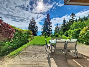 Eine Terrasse mit Tisch und Stühlen, umgeben von üppiger Bepflanzung und hohen Bäumen.