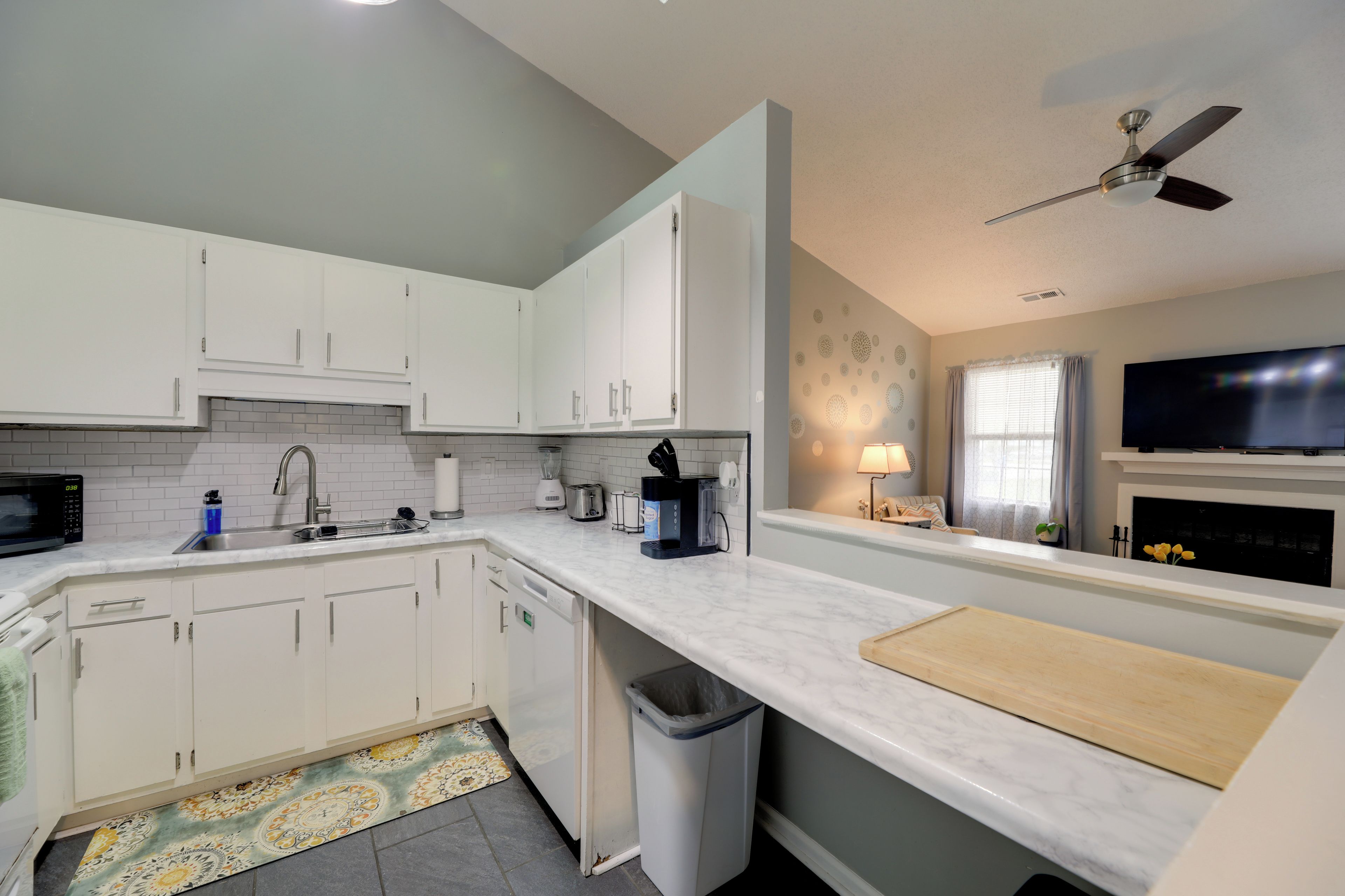 A modern kitchen with white cabinets, a microwave, a sink, and a ceiling fan.