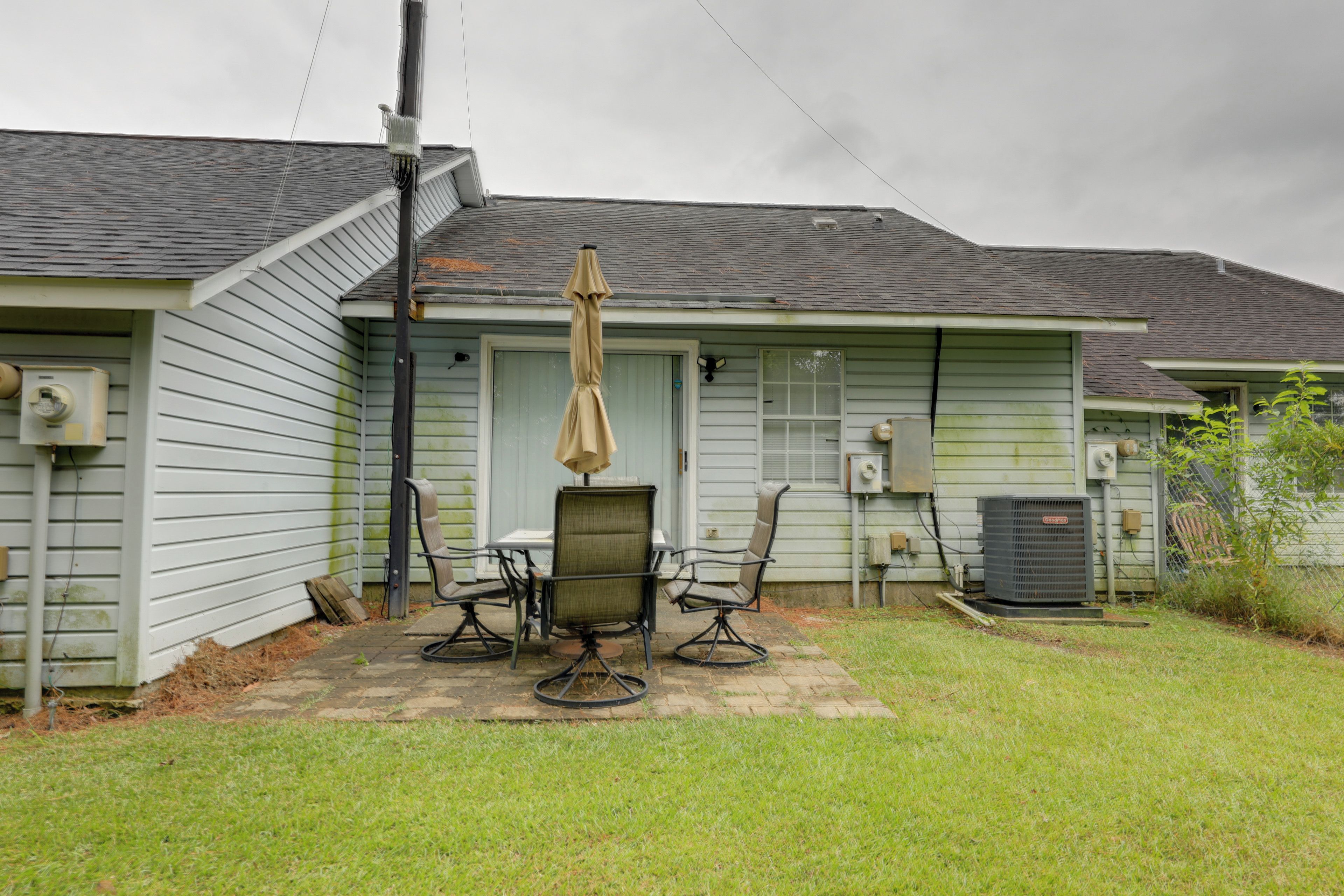 A residential building with a patio area featuring a table and four chairs, an air conditioning unit, and a covered outdoor seating area.