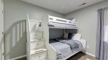 A bunk bed with a desk and drawers, a window with curtains, and a wooden floor.