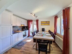 Eine kompakte Küche mit weißen Schränken, einem Esstisch für vier Personen und Blick durch das Fenster.