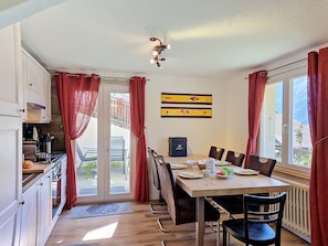 A dining area with a table set for four, chairs, a window with curtains, and a view of the outside. - Apartment Eliane by Interhome (Grächen)
