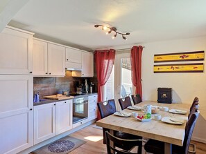 A compact kitchen with white cabinets, a dining table set for four, and a breakfast table with fruit and coffee. - Apartment Eliane by Interhome (Grächen)