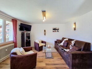 A living room with a sofa, armchairs, a coffee table, a flat-screen TV mounted on the wall, and a fireplace. - Apartment Eliane by Interhome (Grächen)