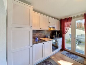 Eine kompakte Küche mit weißen Schränken, einem eingebauten Backofen und einem Fenster mit roten Vorhängen.