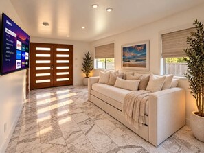 A modern living room with a large flat-screen TV displaying a streaming service interface, a beige sofa with decorative pillows, a potted plant, and a painting on the wall. - Massive 4 Level Villa+Rooftop Marina Views+Hot Tub (San Diego)