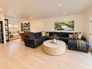 A modern living room with a sectional sofa, a round coffee table, and a foosball table. - Point Loma Sleeps 16 | Rooftop | Beach & Downtown (San Diego)