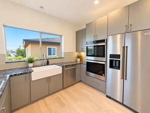 A modern kitchen with stainless steel appliances, a large window, and a view of a house. - Point Loma Sleeps 16 | Rooftop | Beach & Downtown (San Diego)