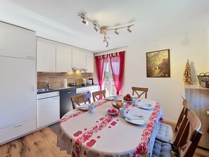 A compact kitchen with white cabinets, a dining table set with plates, cups, and a fruit bowl. - Apartment Eliane by Interhome (Grächen)