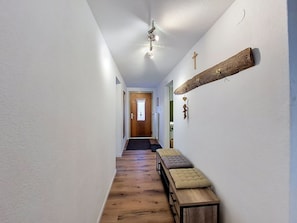 Ein Flur mit einer hölzernen Bank, einem Holzbalken mit Haken und einer Tür am Ende.