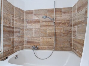 Een badkamer met een badkuip en douche, betegelde wanden en een hoekopstelling.
