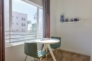 A room with a window, a table, two chairs, and a shelf with decorative items. - Beachfront Extended Escape w/ Workspace! (Santa Monica)