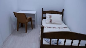 A small, single-bed room with a wooden headboard, a white desk, and a wicker chair. - HINAR HOME (Mardin)