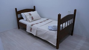 A single bed with a wooden frame, white bedding, and a floral-patterned pillow. - HINAR HOME (Mardin)