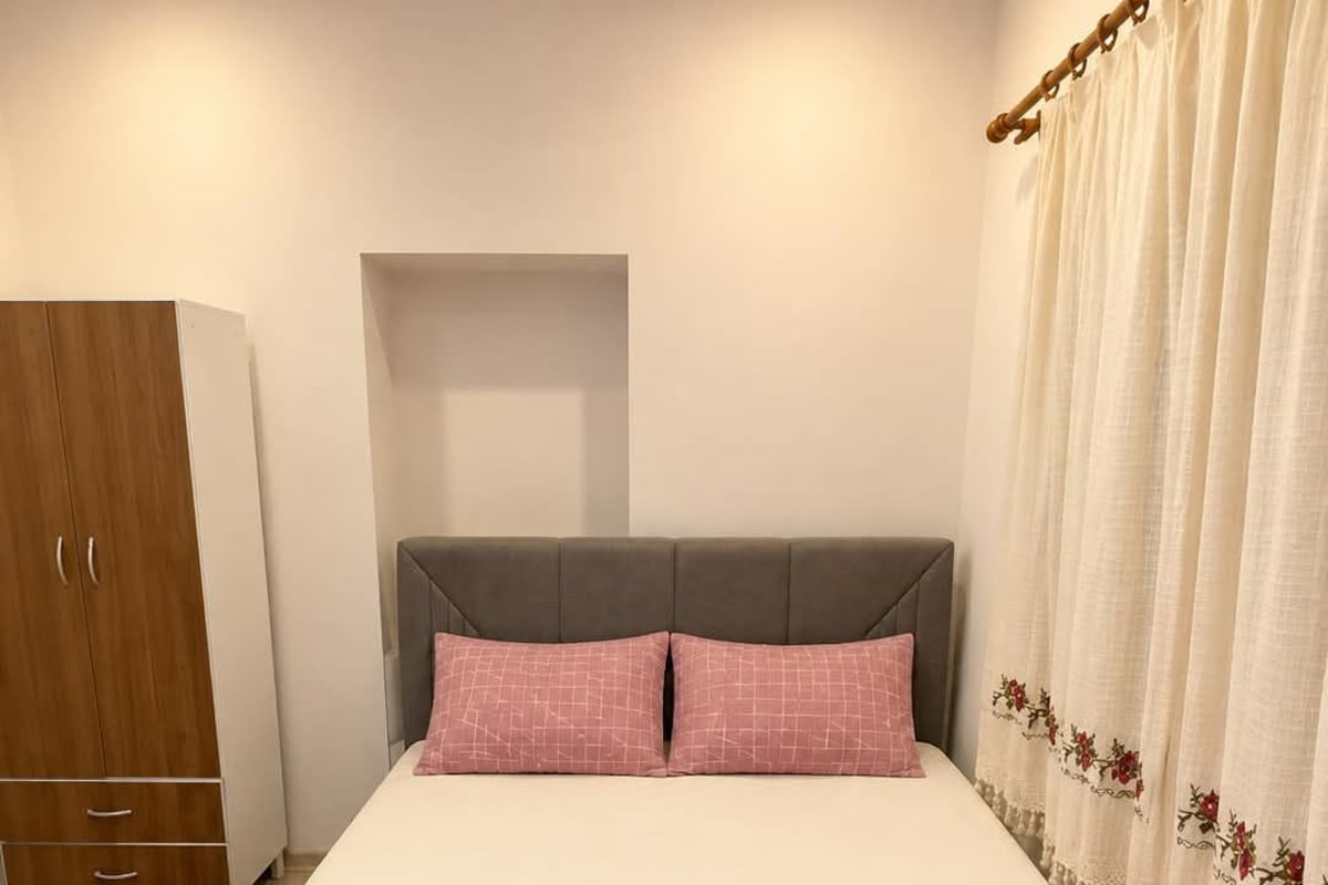 A bedroom with a bed, two pillows, a wardrobe, and a curtain.