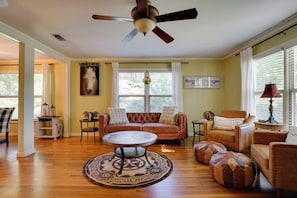 A living room with a brown leather sofa, a round coffee table, and a ceiling fan. - Adorable 1930s Cottage: Downtown + Dog Friendly (Granbury)