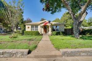 A single-story house with a stone facade, a front porch, and a flag. - Adorable 1930s Cottage: Downtown + Dog Friendly (Granbury)