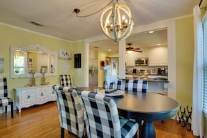 A dining area with a round table, checkered chairs, a chandelier, and a view into the kitchen. - Adorable 1930s Cottage: Downtown + Dog Friendly (Granbury)