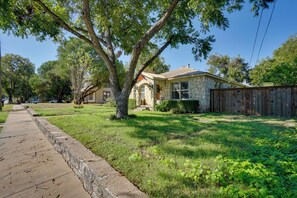 A residential property with a stone facade, a wooden fence, and a well-maintained lawn. - Adorable 1930s Cottage: Downtown + Dog Friendly (Granbury)