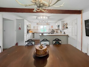 A dining area with a large wooden table, a chandelier with antlers, and a kitchen in the background. - Drum Lang Lodge - UK51054 (Isle of Mull)