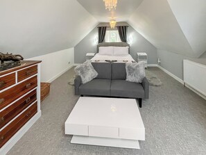 A bedroom with a bed, a dresser, a gray sofa, and a white coffee table. - Drum Lang Lodge - UK51054 (Isle of Mull)