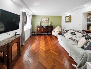A living room with a wooden herringbone floor, a television on a stand, a sofa with patterned cushions, a wooden cabinet, and a painting on the wall. - Drum Lang Lodge - UK51054 (Isle of Mull)