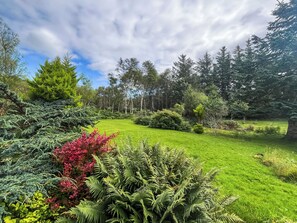 Un jardin luxuriant, avec une grande variété de plantes et d’arbres, une pelouse bien entretenue et un ciel dégagé.