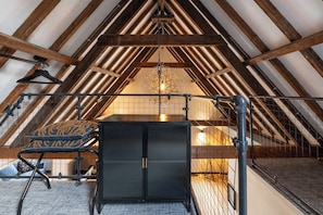 Dormitorio tipo loft con vigas de madera a la vista, una lámpara colgante y un armario negro.