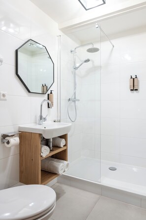 Een moderne badkamer met toilet, wastafel, douche en een douchecabine met glazen wanden.