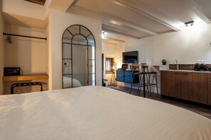 Een hotelkamer met een bed, een bureau, een kitchenette en een badkamer met douche en spiegel.