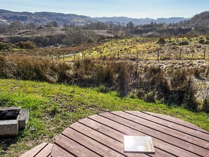 Um deck de madeira com um livro, cercado por um gramado e colinas ao longe.