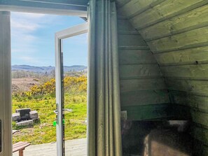 Quarto com uma grande janela, vista para uma paisagem gramada e uma estrutura de metal.