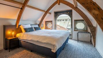 Una camera da letto con soffitto spiovente, un letto, un comodino e due finestre.