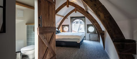 A bedroom with a sloped ceiling, a bed, a window, and a door.