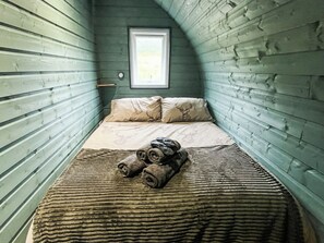A narrow room with wooden walls, a bed with a patterned bedspread, and a window with a view. - 1 bedroom accommodation in Lerags (Lerags)