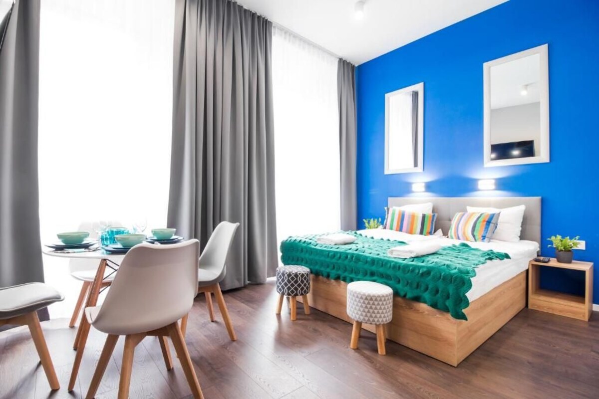 A modern bedroom with a bed, bedside tables, a desk with chairs, and a window with curtains.