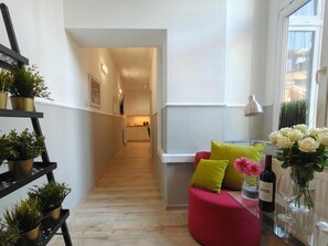 A modern interior with a red sofa, a plant shelf, and a view into a kitchen. - Kings City Sławkowska Apartments (Kraków)
