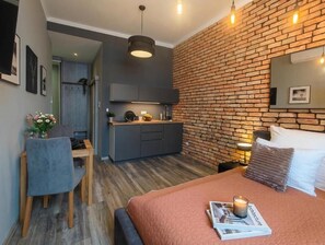 A modern bedroom with a brick wall, a bed with a magazine, a bedside table, and a desk with a chair. - Kings City Sławkowska Apartments (Kraków)