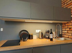 A modern kitchen with a built-in stove, a sink, and a wine bottle on the counter. - Kings City Sławkowska Apartments (Kraków)