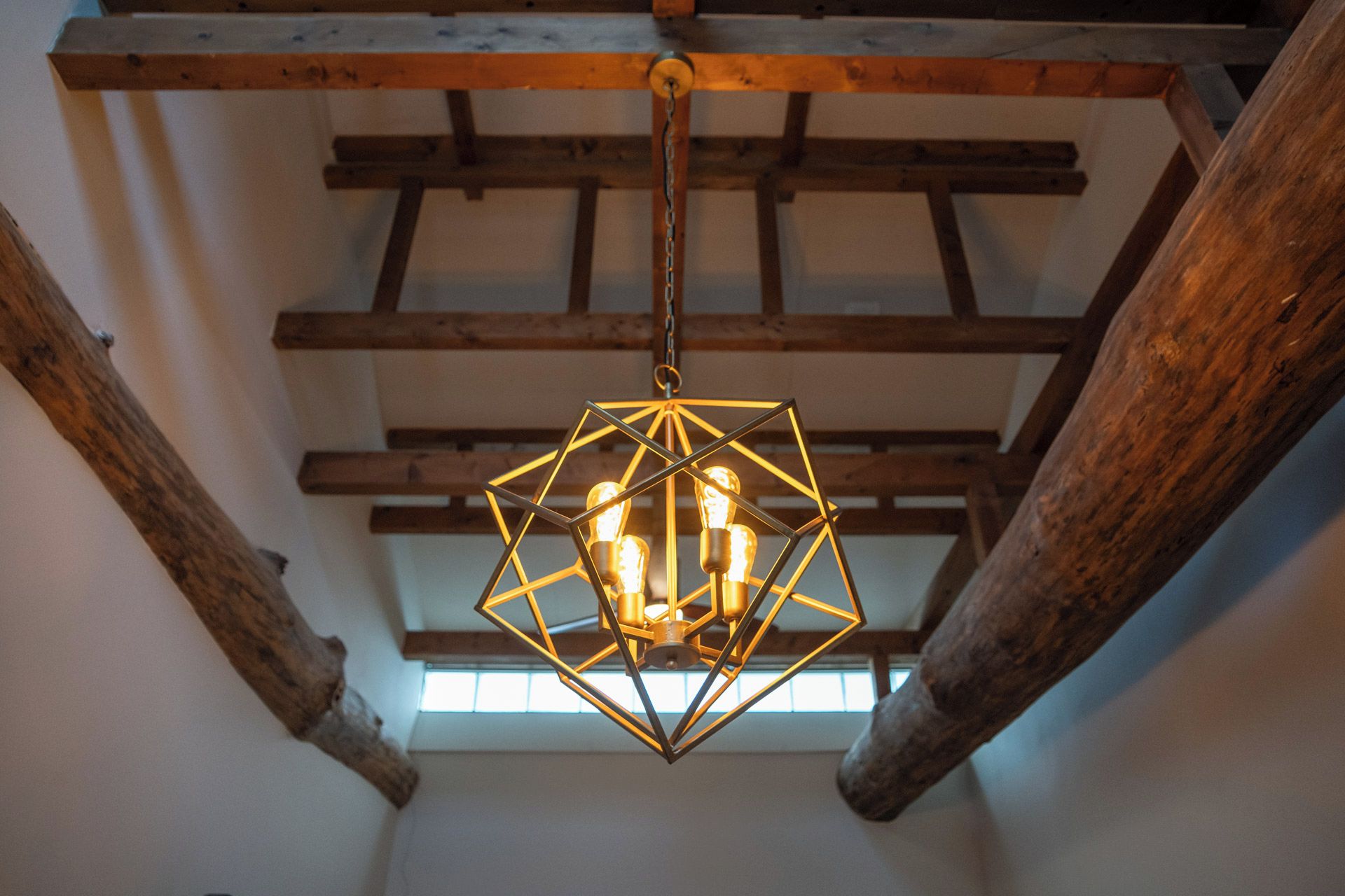 Un lustre métallique hexagonal, dont les ampoules sont apparentes et suspendues à une structure en bois fixée au plafond.