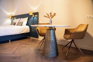 A hotel room with a bed, a round table with a vase, two chairs, and a wall-mounted lamp.