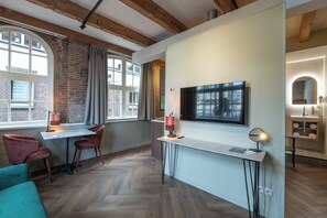 A modern interior with exposed brick walls, a herringbone wood floor, a dining area with a table and chairs, a TV mounted on the wall, and a small kitchenette with a sink and countertop. - Studio Urbain by Grapélli Boutique Hotel (Alkmaar)